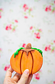Crop anonymous person showing pumpkin cookie decorated with multicolored glaze