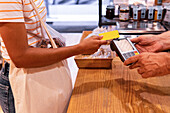 Unrecognizable woman with tote bag using credit card to pay for goods to vendor in zero waste grocery store