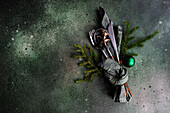 From above table setting for Christmas dinner with dark modern cutlery wrapped in green napkin with fir tree leaves and decor on concrete table
