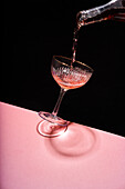 Anonymous person pouring rose sparkling wine into elegant coupe glass against two colored background