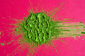 Top view of traditional Japanese powdered matcha tea scattered on bright pink background