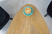 Von oben Tasse heißer Kaffee mit kreativen Latte Kunst serviert auf Teller mit Teelöffel auf Holztisch in modernen Licht Kaffeehaus