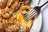 From above appetizing fried eggs with king prawns served on white plate with green herbs and seasoning on towel in light kitchen