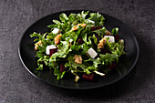 High angle of black plate with tasty beetroot salad with Tofu cheese and green lettuce served on dark background in studio