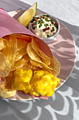 Appetizing fried chips and fish in paper wrapping served on plate with sauce on table with bright sunlight in cafe