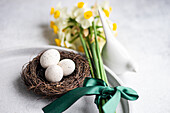 From above easter dinner table set with eggs in the nest and daffodil flowers on concrete background