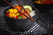 Asiatischer Poke mit Lachs und Reis mit verschiedenen Gemüsesorten, serviert in einer Schüssel auf einem Tisch mit Stäbchen in einem Restaurant