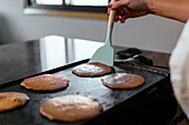 Side view of cropped unrecognizable adult woman standing at counter and flipping pancakes with spatula while making breakfast