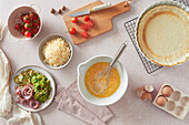 Top view of various fresh ingredients for quiche placed near empty crust on table in kitchen at home