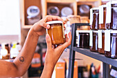 Cropped unrecognizable female vendor arranging glass jars with various jam sauces on shelf during work in eco friendly grocery shop