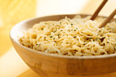 Close-up of bowl of delicious noodles with seasoning placed on yellow background with wooden chopsticks in light room