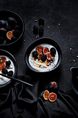 Appetitanregendes gesundes Frühstück bestehend aus Joghurt, frischen Feigen und Brombeeren, bestreut mit Samen und Nüssen auf einem schwarzen Tisch von oben