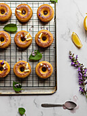 Top view of tasty donuts on cooling rack with leaves between blooming lavender sprigs on marble surface