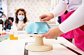 Crop unrecognizable woman decorating cake with glaze while demonstrating skills for colleagues in confectionery