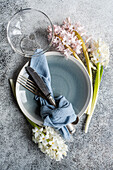 From above spring table setting with hyacinth flower near ceramic plate and cutlery on grey concrete table for festive dinner