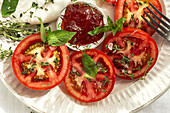 Top view of slices of fresh tomato and mozzarella cheese with sauce and herbs served on plate on table in daylight