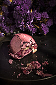 From above bouquet of fresh violet flowers placed on marble table near plate with crushed macaroon in morning.
