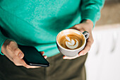 Adult male with cup of aromatic coffee text messaging on cellphone in light house
