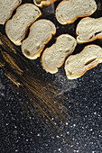 Top view of pieces of white bread near knife and wheat spikes on wooden board