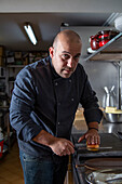 Focused male chef in uniform cutting fresh bun on cutting board while standing at counter in light kitchen of restaurant