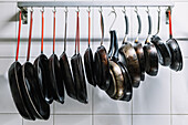 Various sized metal pans hanging in row on hooks attached to railing near white tiled wall