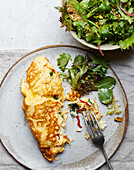 Draufsicht auf appetitlichen vegetarischen Salat mit grünen Kräutern und Omelett auf Teller mit Gabel