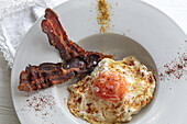 Overhead view of tasty eggs with fried bacon strips on plate