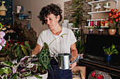 Female gardener watering green plants in floral store
