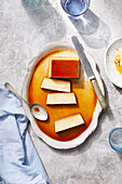 Ansicht von oben auf einen leckeren hausgemachten Flan, spanisches Dessert mit Karamellsauce, serviert auf einem großen Teller mit Löffel und Messer auf einem Marmortisch