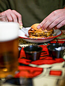 Crop anonymous man in t shirt sitting at table with appetizing burger and beer in restaurant