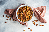 Ceramic bowl with organic almonds on white concrete background