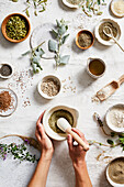 Top view of anonymous person grinding spices on table near assorted aromatic herbs and seeds