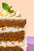 Close up of slice of tasty sweet carrot sponge cake with cream decorated with mint leaf served on plate with spoon on table on colorful background