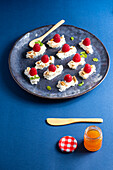 Leckeres appetitliches Dessert mit Sahne und Himbeeren, serviert mit Minzblättern und Nüssen auf einem Teller neben einem Glas Honig mit Löffel und Messer