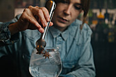 Cropped soft focus of focused female barkeeper adding star anise into wineglass with alcoholic gin and tonic cocktail during work in bar