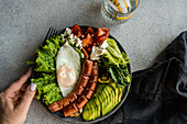 healthy ketogenic lunch plate with vegetables, fried egg and sausages served on the concrete plate