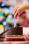 Crop unrecognizable woman with knife aligning chocolate cake while cooking in professional bakery