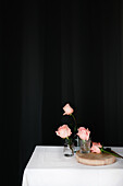 Rosa Rosen in Glasvasen auf dem Tisch vor schwarzem Hintergrund