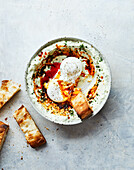 Top view of delicious homemade butter spread with spicy oil on plate with herbs and sliced bread placed on table