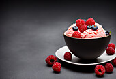 Delicious pink ice cream scoop decorated with raspberries and blueberries placed in black bowl against gray background