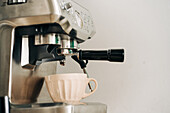 Keramiktasse auf Edelstahl-Kaffeemaschine mit Siebträger in Küche auf weißem Hintergrund