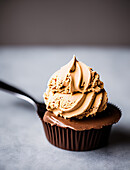 Leckerer süßer gebackener Schokoladen-Cupcake mit Schlagsahne auf grauem Hintergrund im Studio