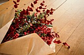 From above of festive stylish decorative Christmas bouquet with twigs of eucalyptus and bright red branches with berries placed on wooden table in room