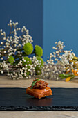 Delicious appetizer in square bite decorated with green leaf served on black board near blooming gypsophila