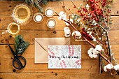 Top view of Christmas composition with colorful postcard with inscription Feliz Navidad placed near burning candles and cups of tea on wooden table decorated with colorful branches of plants