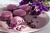 Köstliche violette Makronen auf einem Teller mit zarten Blumen auf einem Tisch im Sonnenlicht