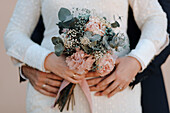 Anonymer Bräutigam umarmt elegante Braut in weißem Hochzeitskleid mit zartem Blumenstrauß