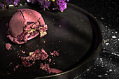 From above bouquet of fresh violet flowers placed on marble table near plate with crushed macaroon in morning.