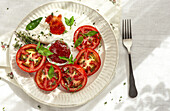 Top view of slices of fresh tomato and mozzarella cheese with sauce and herbs served on plate on table in daylight