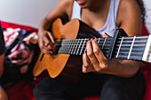 Cropped unrecognizable woman sitting on bean bags on cozy light terrace of apartment and playing guitar